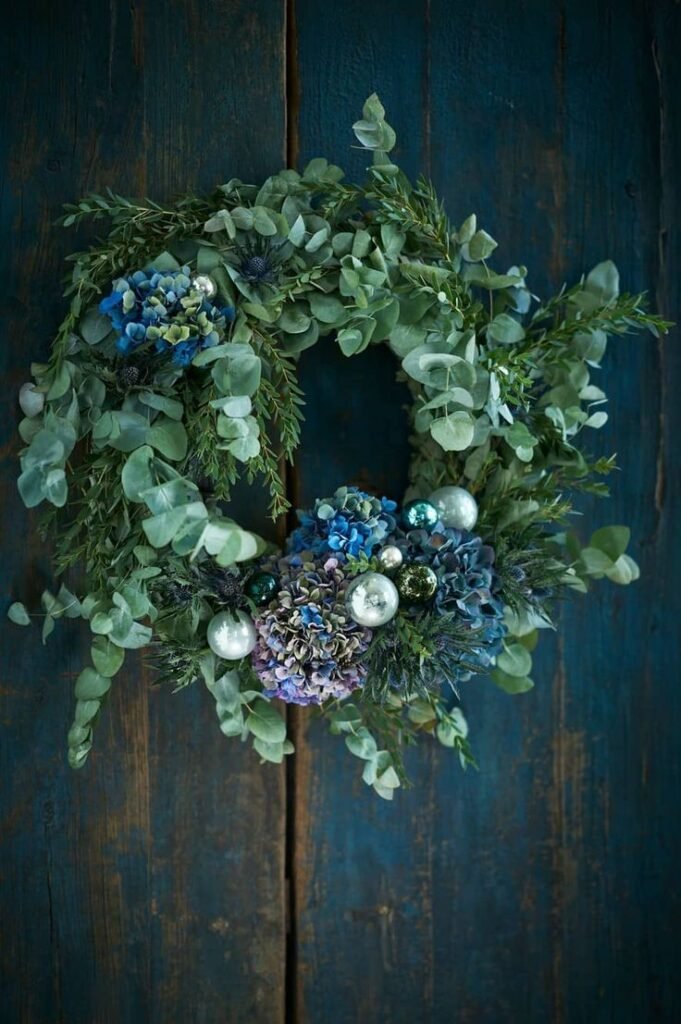 Couronne de Noël art floral en eucalyptus avec fleurs bleus et violettes sur porte bleue