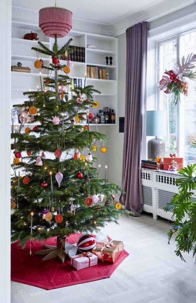 Déco maison avec sapin de Noël avec oranges séchées bougies et boules rouges dans pièce classique chic_