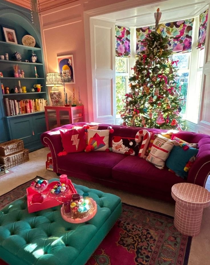 Déco sapin de Noël 2025 avec boules de Noël rouges dans salon coloré éclectique avec canapé rose