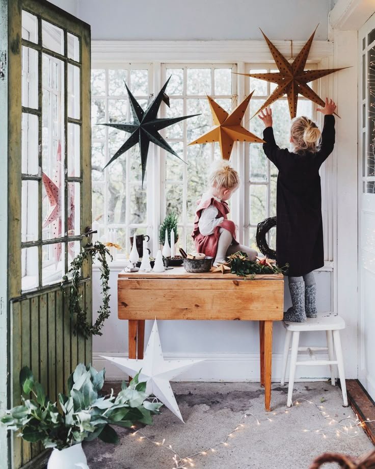Enfant accrochant des etoiles de Noel derriere une fenetre au dessus console en bois