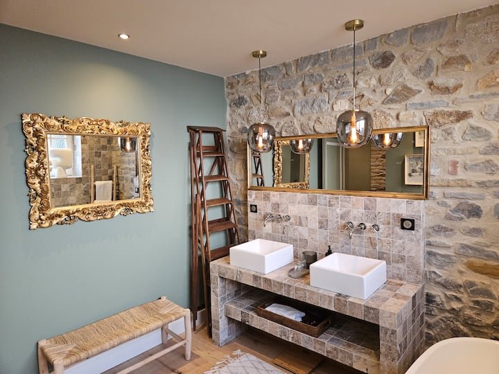 Salle de bain en pierre avec petit banc en bois et miroir doré dans duplex 75m2 Vichy